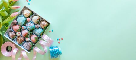 Blue handmade chocolate covered strawberries, flowers and decoration for cooking dessert on green background with free space for textの写真素材