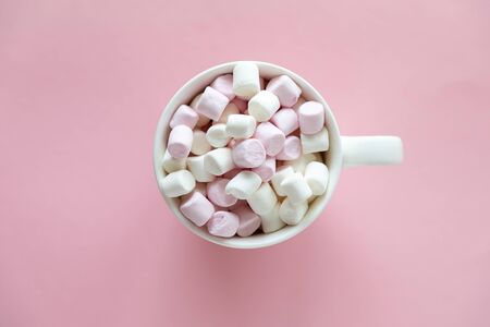 Pink and white mini marshmallows in the cup with hot chocolate on pink background with free space...