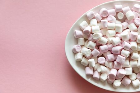 Pink and white mini marshmallows in a white plate on pink background with free space for textの写真素材