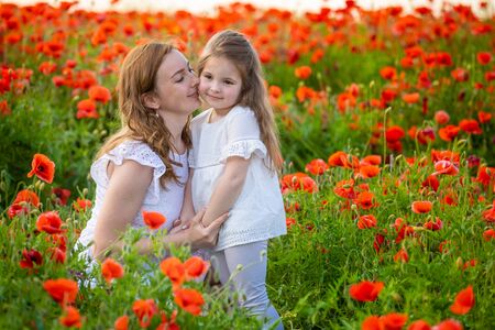 Beautiful mother and her daughter in spring poppy flower field in Czech republicの写真素材