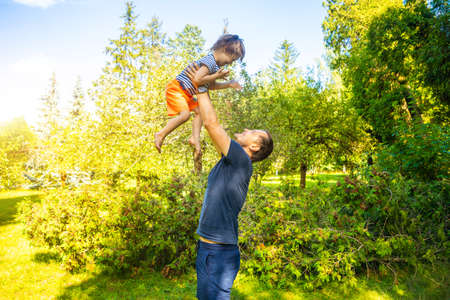Portrait of cute baby boy with Down syndrome playing with dad in summer day on natureの写真素材