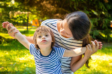 Portrait of cute baby boy with Down syndrome playing with mother in summer day on natureの写真素材