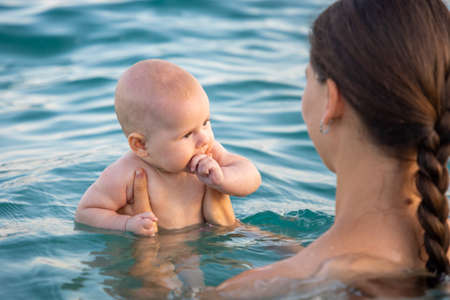 Beautiful young woman with her daughter little baby girl swimming in the sea at sunset time. Woman...