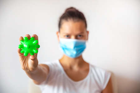 Young woman in medicine mask with green plastic ball as virus in the hand on the white background,...