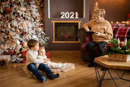 Grandmother reading book to grandchildren near Christmas tree at decorated home, Happy New year 2021
