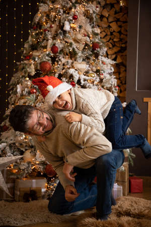 Father and son in christmas hats are enjoying near christmas tree in modern decorated home, Happy New yearの写真素材