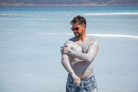 Happy and funny male tourist takes smears natural cosmetic clay to his body on Salda lake, Turkeyの写真素材