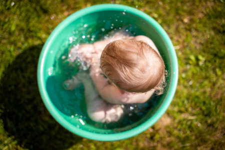 Baby girl flop in a basin with water on home backyard in summer timeの写真素材
