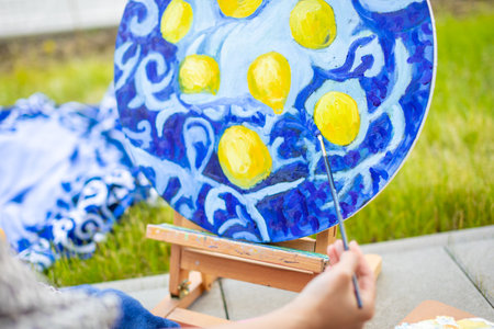 View of hand of young woman painting picture of lemons on blue blanket in home terrace. High quality photoの写真素材