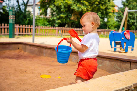Adorable toddler girl playing with sand on sandbox in playgroundの写真素材