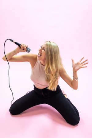 Beautiful young woman with microphone singing on pink background