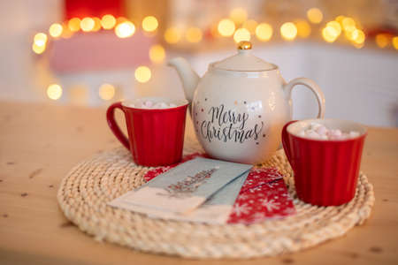 White Ceramic TeaPot with text Merry Christmas and cups with marshmallows on xmas bokeh backgroundの写真素材