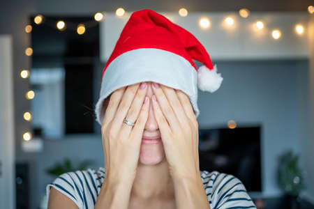 Happy young woman in santa hat smiling at lights decorated homeの写真素材