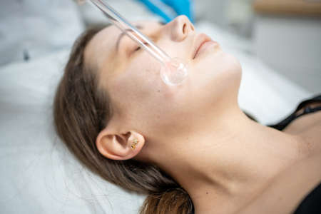 Beautician uses the darsonval device on the clients face. Professional skin care in the salon. The...