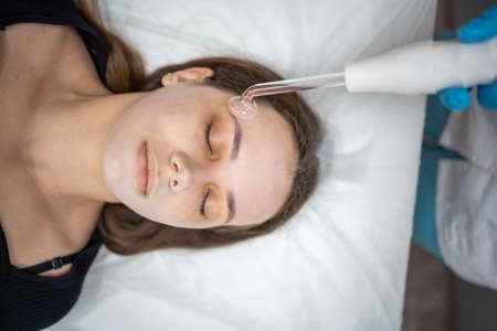 Beautician uses the darsonval device on the clients face. Professional skin care in the salon. The...