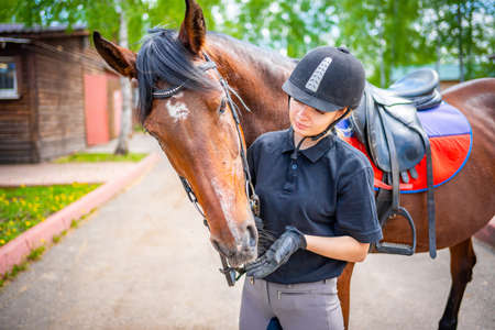 Lovely young woman wearing helmet stroking to her brown horse