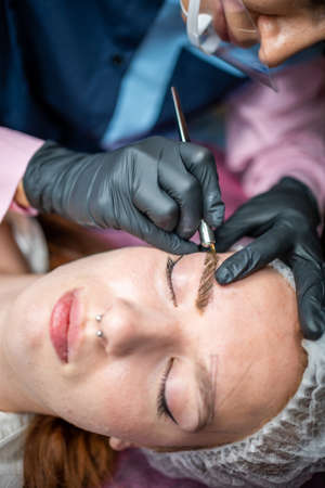 Procedure of eyebrow microblading. A master in black gloves is doing a blending needle of models...