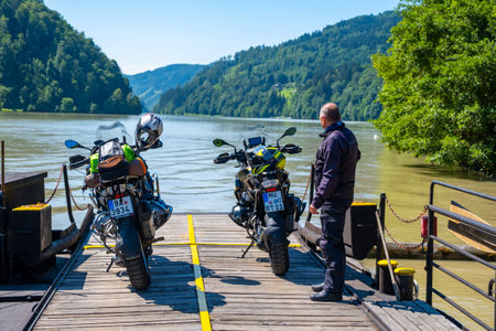 Alps, Austria - July 3, 2022: Small ferry with motorcycles on board crossing the river in the Alps mountains of Austriaのeditorial素材
