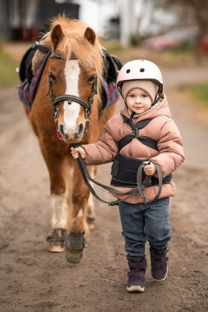 Little girl in protective jacket and helmet with her brown pony before riding Lesson. High quality photoの写真素材