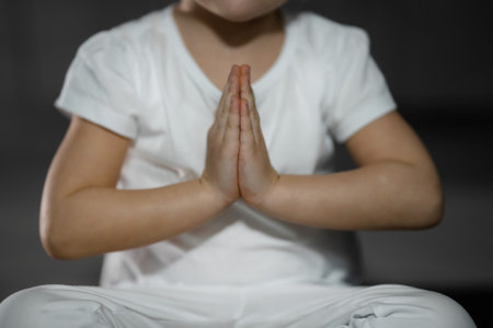 Three years old little girl meditating in a lotus pose on a gray background in dark room. High quality photoの写真素材
