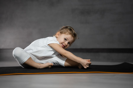 Little cute girl practicing yoga pose on grey background in dark room. High quality photoの写真素材