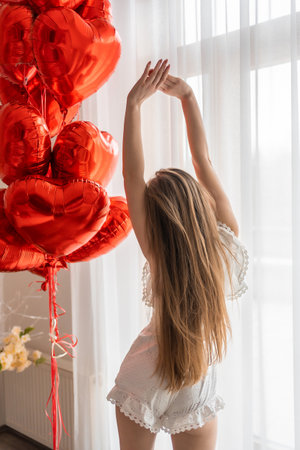 Beautiful young girl at home in bedroom in the morning enjoy valentines day celebration with heart shaped balloons. High quality photoの写真素材
