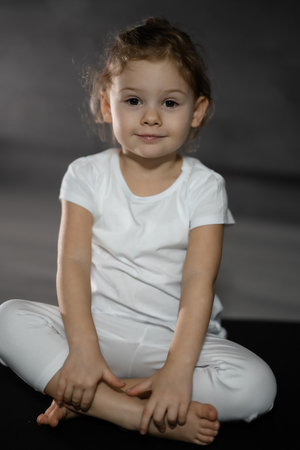 Little cute girl practicing yoga pose on grey background in dark room. High quality photo