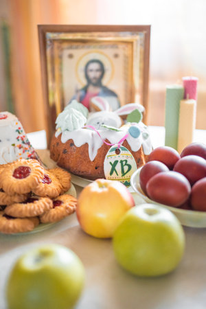 Easter cake with painted eggs, apples and cookies on table in home kitchen. Church icons and candle on background. Orthodox religion theme. High quality photoの写真素材