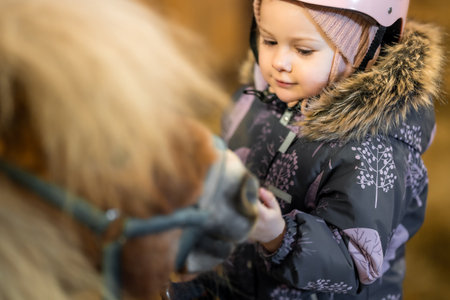 Portrait of little girl in protective jacket and helmet with her brown pony before riding Lesson. High quality photoの写真素材