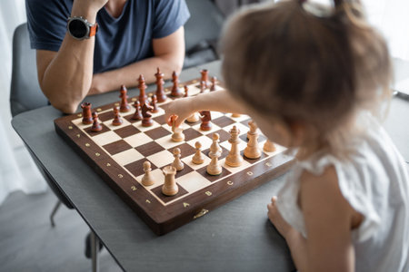Little girl playing chess with her father at the table in home kitchen. The concept early childhood development and education. Family leisure, communication and recreation. High quality photoの写真素材