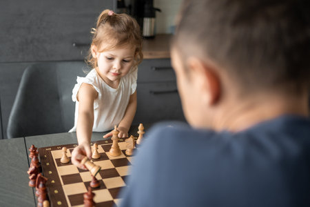 Little girl playing chess with her father at the table in home kitchen. The concept early childhood development and education. Family leisure, communication and recreation. High quality photoの写真素材