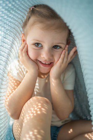 Little girl have a fun under blue knitted plaid in sunny morning. High quality photoの写真素材