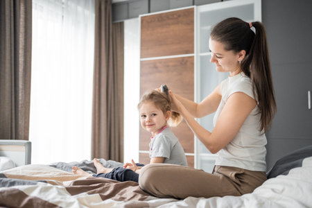 Young mother combs her little daughters hair while sitting in bed in the morning. High quality photo