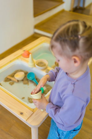Little girl playing with kinetic sand and wooden toys. Sensory development and experiences, themed activities with children, fine motor skills development. High quality photoの写真素材