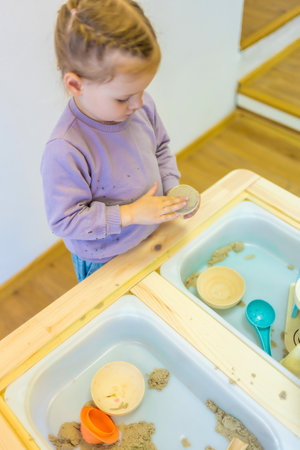 Little girl playing with kinetic sand and wooden toys. Sensory development and experiences, themed activities with children, fine motor skills development. High quality photoの写真素材