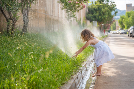 Funny laughing little girl running though garden sprinkler playing with water splashes having fun in sunny hot summer vacation day. High quality photoの写真素材