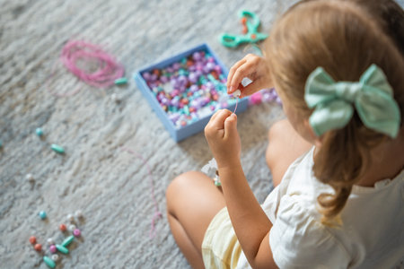 Little girl making wooden beads bracelet at home living room. Childrens creativity and the development of fine motor skills. High quality photoの写真素材