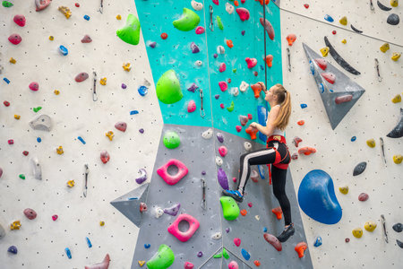 Rock climber young woman hanging on colored hooks on climbing artificial wall indoors of sport...
