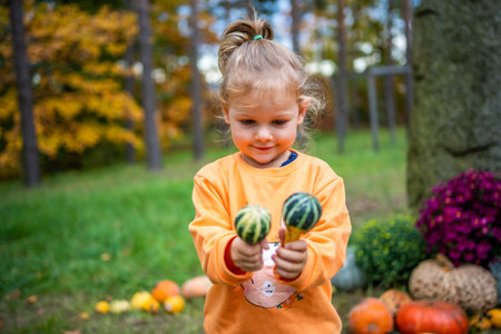 Cute little girl having fun with huge pumpkins on a pumpkin patch. Kid picking pumpkins at country farm on warm autumn day in Prague. Family time at Thanksgiving and Halloween. High quality photoの写真素材