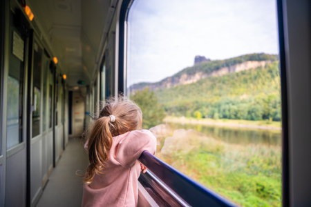 Little girl looking out train window outside, while it moving. Traveling by railway, Europe. High quality photoの写真素材