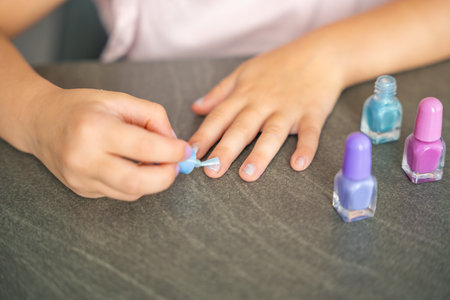 Top view of Hands of little girl doing manicure and painting nails with colorful pink, blue and purple nail polish at home. High quality photoの写真素材