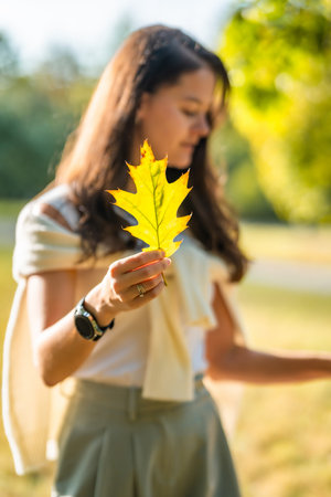 Portrait of young woman with autumn leaf in autumn park in Prague, Europe. Focus on autumn leaf....