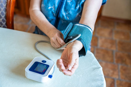 Senior woman start to check blood pressure level at home, older female suffering from high blood pressure sitting and using a pulsometer, tonometer. High quality photoの写真素材