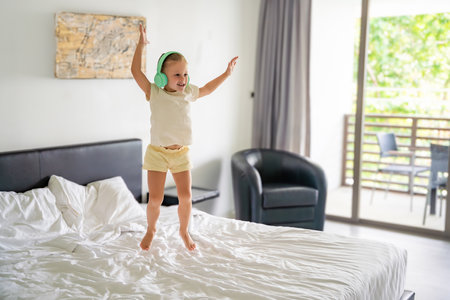 Little girl listening to the music with kids headphones and dancing on bed. High quality photoの写真素材