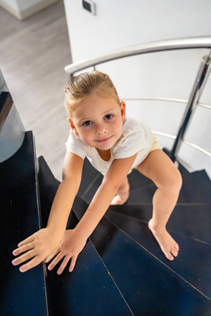 Portrait of little girl going up the stairs at home, child climbing spiral staircase. Dangerous situation at home. Child safety concept. . High quality photoの写真素材