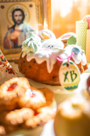 Easter cake with painted eggs, apples and cookies on table in home kitchen. Church icons and candle...