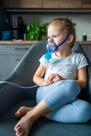 Cute little girl are sitting and holding a nebulizer mask leaning against the face, airway treatment concept. High quality photoの写真素材