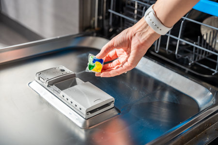Woman hand putting detergent, multifunction tablet into the dishwasher. Household chores, duties with a modern kitchen appliance. High quality photoの写真素材