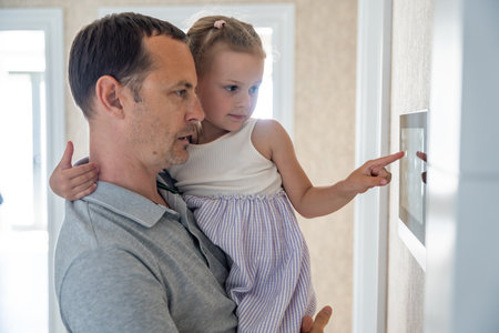 Daughter in her father using tablet panel application for control smart home living. Wireless device...