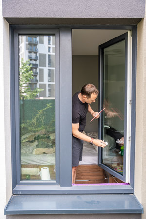 Young man cleans the windows in the house. He splashes detergent, rubs and removes water at the...